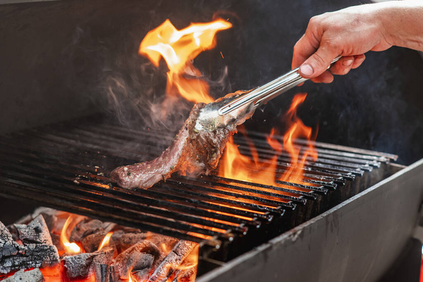 A man fries grilled beef steak with flames - Zdjęcie, obraz