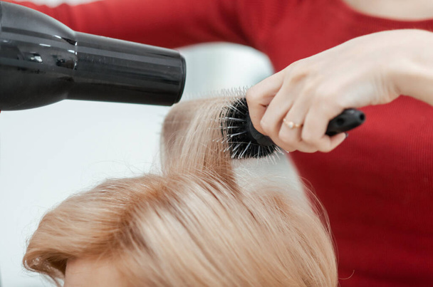 El trabajo de un peluquero. El maestro seca el cabello del cliente usando cepillado. Primer plano de las manos y la herramienta
 - Foto, Imagen