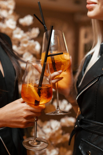 De meisjes aan de bar hangen glazen met een Aperol Spritz cocktail. Close-up van de handen - Foto, afbeelding