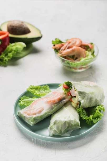 Spring rice paper roll with shrimp, avocado, paprika, lettuce and cottage cheese on a bright plate on a white background. Side view with a copy space. Vertical orientation. - Fotografie, Obrázek