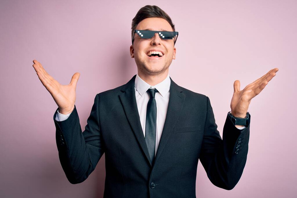 Jonge knappe blanke zakenman draagt grappige bandieten levensbril die gek en gek vieren voor succes met opgeheven armen en gesloten ogen schreeuwend opgewonden. Winnaars concept - Foto, afbeelding