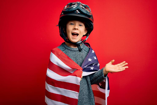 Młody patriotyczny dzieciak ubrany w amerykańską flagę i kask motocyklowy 4 lipca bardzo szczęśliwy i podekscytowany, zwycięzca świętuje zwycięstwo krzycząc z wielkim uśmiechem i podniesionymi rękami - Zdjęcie, obraz