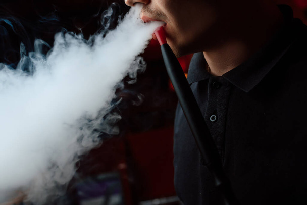 Egy férfi vízipipát szív, szájfeltétet tart a szájához és füstöt lélegez ki. - Fotó, kép