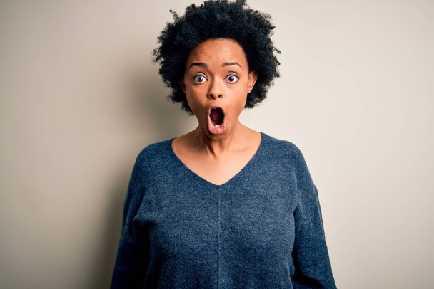 Jeune belle afro afro-américaine aux cheveux bouclés portant un pull décontracté effrayé et choqué par la surprise et l'expression étonnante, la peur et le visage excité
. - Photo, image