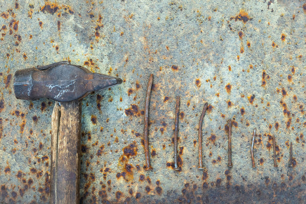 Top view of the old hammer and rusty nails lie in a row on a rusty metal background. Conceptual photo - Photo, Image