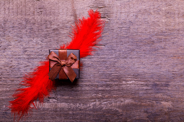 Caixa de presente com pluma vermelha na velha mesa de madeira rústica para o dia dos namorados. Espaço de cópia para texto
. - Foto, Imagem