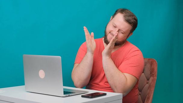 ピンクのTシャツを着た若い幸せなビジネスマンは、ノートパソコンで働き、緑の画面に手を閉じます。ノートパソコンを覗き込む男の肖像画。事務所の机で働いてる男. - 写真・画像