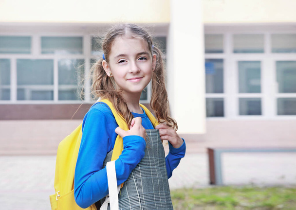Caucasian child girl with yellow backpack at school yard background..Back to school.Pupil portrait outdoors september 1.Schoolkid education. - Fotó, kép