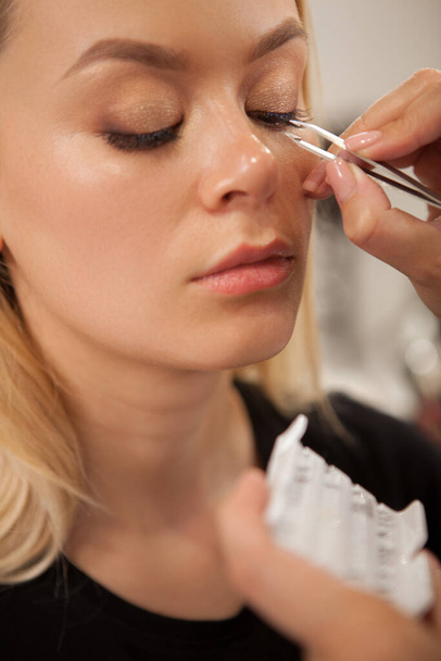 close vertical de uma mulher bonita recebendo pestanas falsas coladas pelo artista de maquiagem profissional
 - Foto, Imagem