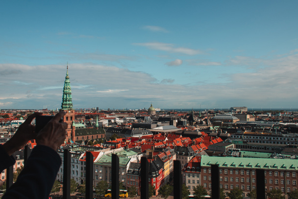 Danimarka 'nın arka planında Kopenhag şehrinin binalarıyla akıllı telefonlu fotoğraf çeken bir adamın görüntüsü.  - Fotoğraf, Görsel