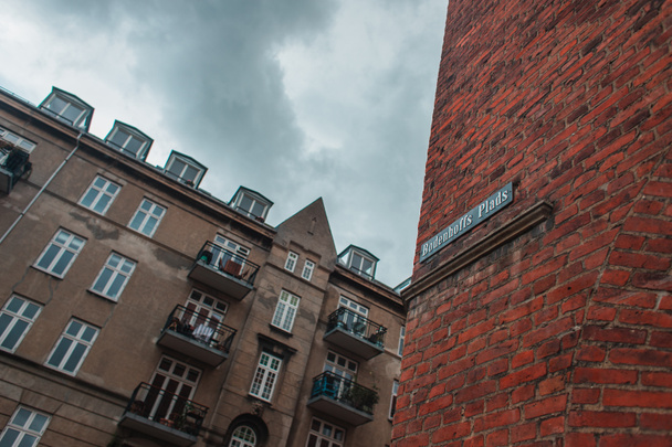 Χαμηλή γωνία άποψη της πινακίδας με το όνομα του δρόμου στην πρόσοψη τούβλο του κτιρίου και συννεφιασμένο ουρανό στο παρασκήνιο στην Κοπεγχάγη, Δανία  - Φωτογραφία, εικόνα