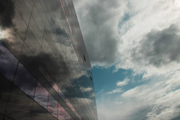 COPENHAGEN, DENMARK - APRIL 30, 2020: Low angle view of glass facade of Black Diamond Royal Library with cloudy sky at background, Copenhagen, Denmark   - Фото, изображение
