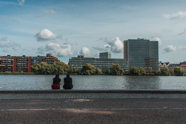 Mensen zitten op de promenade in de buurt van kanaal met gebouwen en bewolkte lucht op de achtergrond, Kopenhagen, Denemarken  - Foto, afbeelding