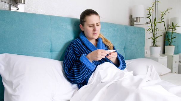 Sick young woman feeling unwell measuring temperature - Fotó, kép