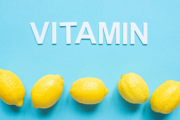 vista superior de limones amarillos maduros y palabra vitamina sobre fondo azul
 - Foto, imagen