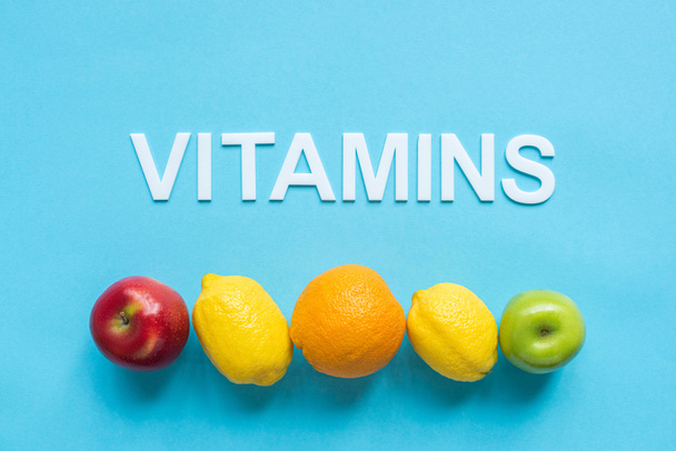 horní pohled na zralé ovoce v souladu a slovo vitamíny na modrém pozadí - Fotografie, Obrázek