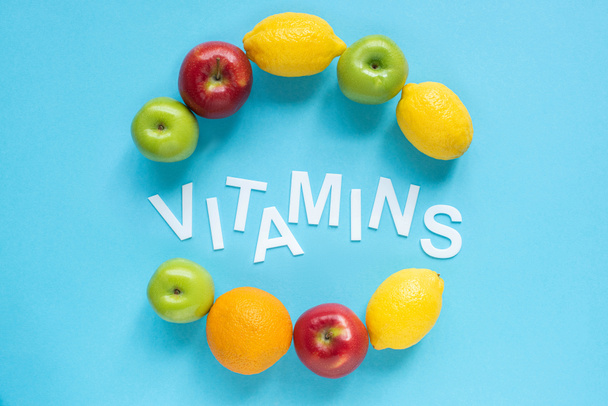bovenaanzicht van rijp fruit rond woord vitaminen op blauwe achtergrond - Foto, afbeelding