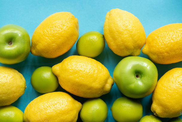 Mavi arka planda olgun sarı limonlar, yeşil elma ve limonlar. - Fotoğraf, Görsel