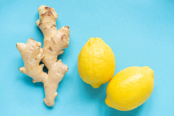 top view of ripe yellow lemons and ginger root on blue background - Foto, Imagen