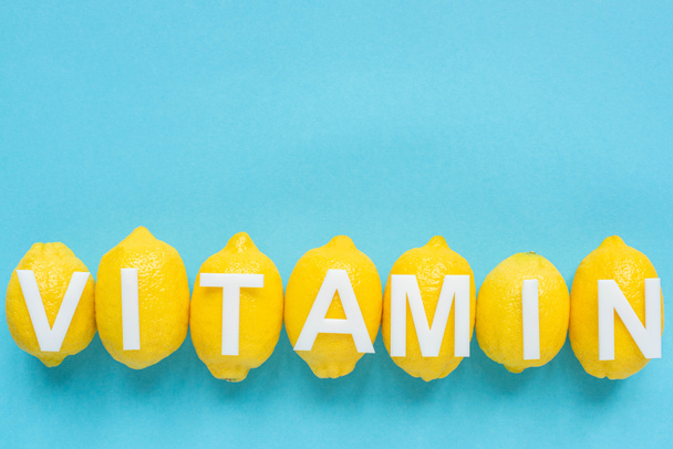 bovenaanzicht van rijpe gele citroenen en woord vitamine op blauwe achtergrond - Foto, afbeelding