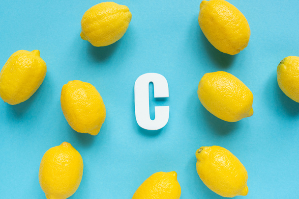 top view of ripe yellow lemons and letter C on blue background - 写真・画像