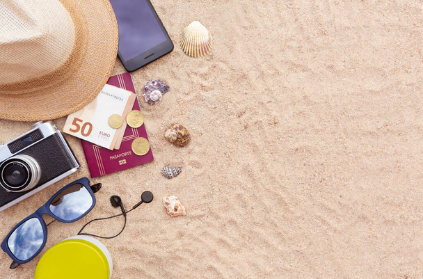 Wat strandspullen, een paspoort en wat geld, een smartphone, hoed, camera en zonnebril op het zand. Ruimte voor tekst. Vakantie, zomer en strand concept. - Foto, afbeelding