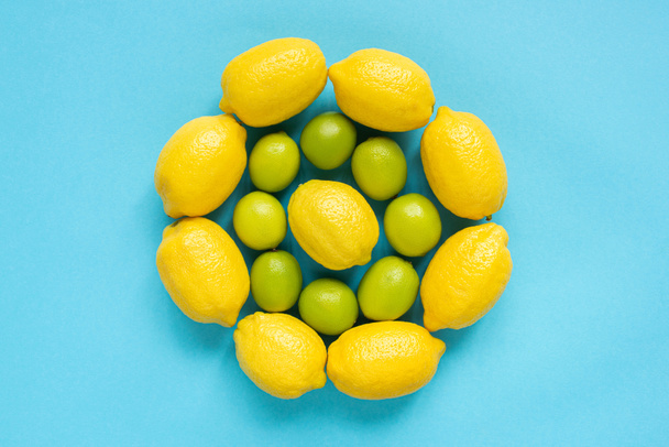 top view of ripe yellow lemons and limes arranged in circles on blue background - Φωτογραφία, εικόνα