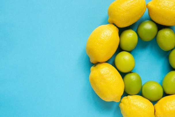 top view of ripe yellow lemons and limes arranged in circles on blue background - Photo, Image