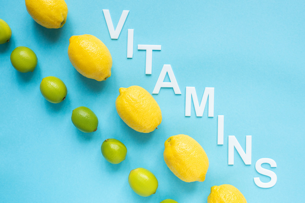 tendido plano con limones amarillos maduros, limas verdes y vitaminas palabra sobre fondo azul
 - Foto, Imagen