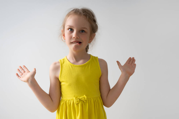 Angstig klein meisje dat haar handen opsteekt in een hulpeloos gebaar en zenuwachtig op haar onderlip bijt. taille-up studio portret geïsoleerd op wit - Foto, afbeelding