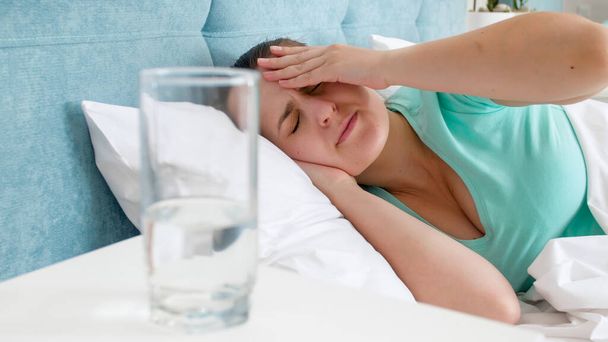 Portret młodej kobiety z bólem głowy leżącej w łóżku - Zdjęcie, obraz