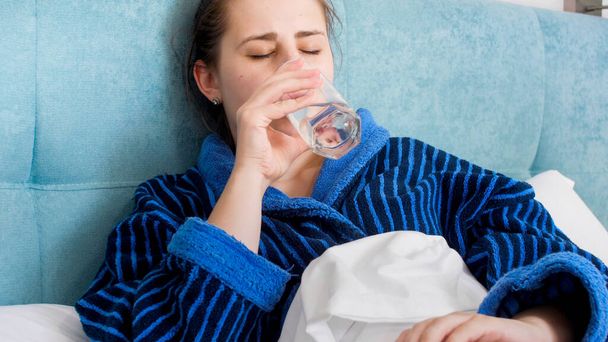 Portrait of sick woman lying in bed and drinking water - Photo, Image