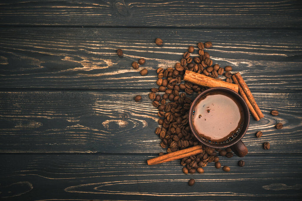 Kopje koffie met gebrande bonen en kaneel op een houten tafel. bovenaanzicht - Foto, afbeelding