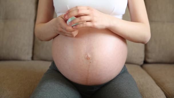 nainen voitelee kosteuttaa raskaana vatsa kerma venyttää markkaa kotona sohvalla. Body kosmeettisia anti-venytetty iho hidastettuna - Materiaali, video