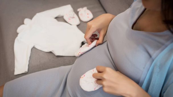 Joven atractiva embarazada mujer asiática preparando ropa para su bebé en casa
. - Foto, imagen