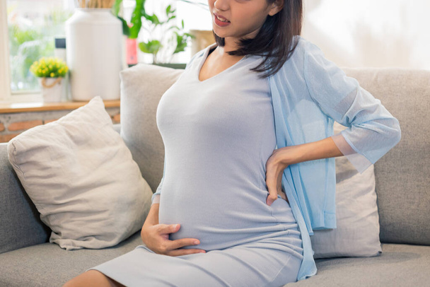 Young Asian beautiful pregnant woman touching her tummy, getting back pain. - Photo, image