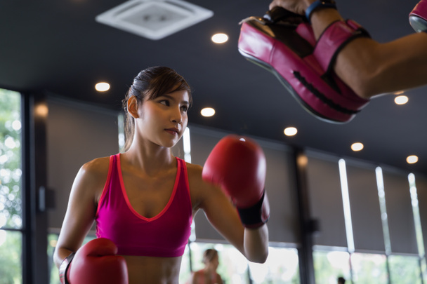 Νεαρή υγιής Ασιάτισσα κάνει πυγμαχία με εκπαιδευτή στο γυμναστήριο, τον αθλητισμό και την ψυχαγωγία έννοια δραστηριότητα. - Φωτογραφία, εικόνα
