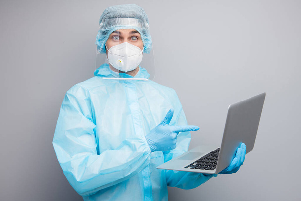 Photo of guy expert doc virology center hold notebook direct finger screen chatting patients online wear respirator hazmat uniform suit plastic face shield isolated grey color background - 写真・画像