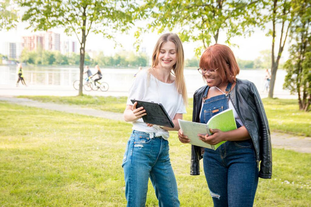 Two female students communicate in the park. Cheerful conversation riznonatsionalnyh girls - Foto, immagini