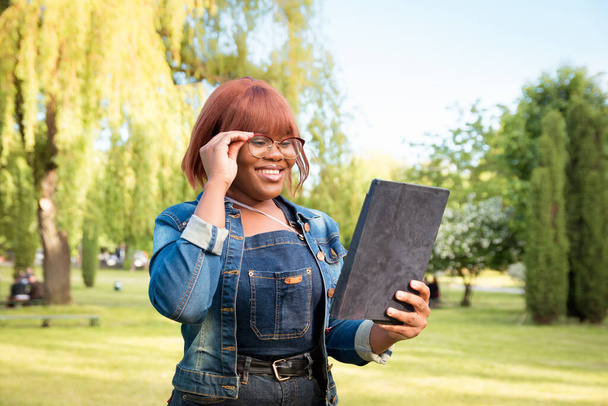 A fekete diáklány modern kommunikációs eszközökkel kommunikál. Egy nő portréja egy táblával a kezében a szabadban. - Fotó, kép
