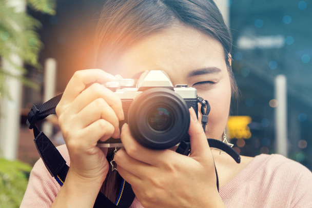 pretty cool young Asian woman with retro film camera or mirrorless camera in modern garden open mall.young woman holding mirrorless camera in vintage tone; - Foto, Imagem