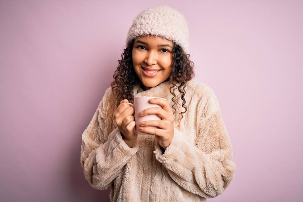 Jovem mulher bonita com cabelo encaracolado bebendo caneca de café sobre fundo rosa isolado com um rosto feliz de pé e sorrindo com um sorriso confiante mostrando dentes
 - Foto, Imagem