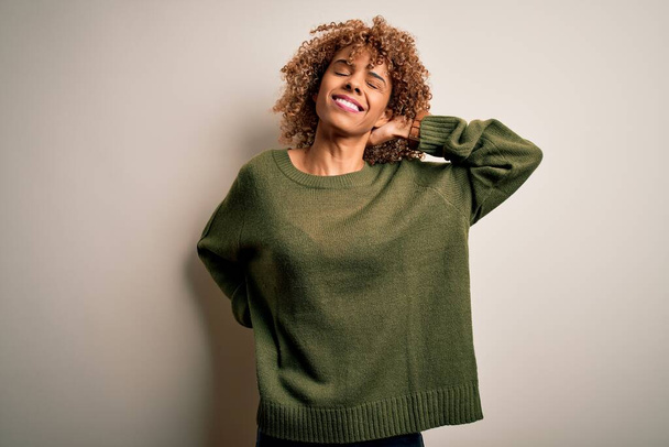 Beautiful african american woman with curly hair wearing casual sweater over white background Suffering of neck ache injury, touching neck with hand, muscular pain - Foto, immagini