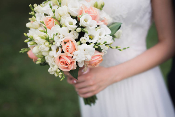νύφη κρατώντας γαμήλιο μπουκέτο λουλουδιών σε εξωτερικούς χώρους. ρομαντικό φόντο - Φωτογραφία, εικόνα