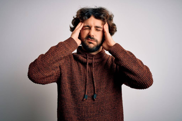 Young handsome man with beard wearing casual sweater standing over white background suffering from headache desperate and stressed because pain and migraine. Hands on head. - Foto, Bild