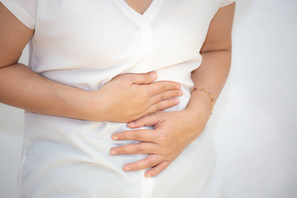 Kuva aasialaisesta naisesta, joka pitelee kättään vatsassaan mahakivun, vatsakivun ja valkoisella pohjalla olevien elintarvikeperäisten infektioiden vuoksi. - Valokuva, kuva