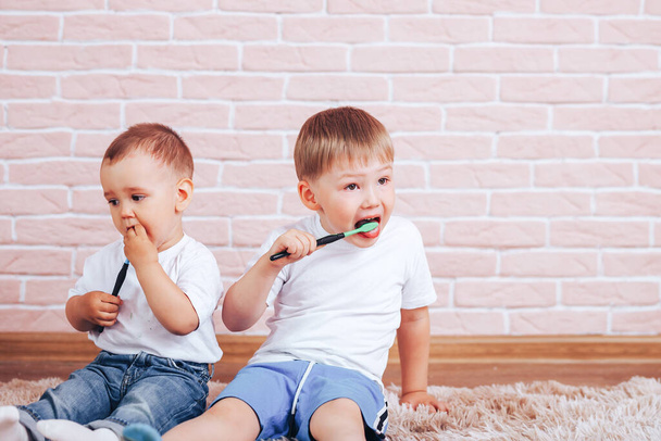 Pienet lapset harjaavat hampaansa hammasharjoilla istuessaan lattialla, huolehtien hampaistaan lapsuudesta lähtien.. - Valokuva, kuva