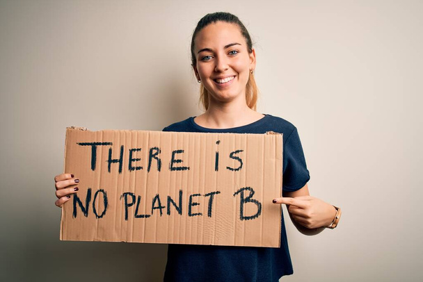 Young beautiful blonde woman with blue eyes asking for protect planet holding banner very happy pointing with hand and finger - Photo, Image
