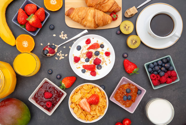 Aamiainen voikroissantilla, maissihiutaleita sekoitettuna kokonaisiin jyviin ja mansikan, mustikan, vadelman ja kiivin ryhmähedelmiin, C-vitamiinia ja terveellistä ruokaa puupöydällä - Valokuva, kuva