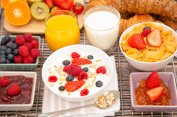 Desayuno con cruasán de mantequilla, copos de maíz mezclados con granos integrales y fruta de grupo de fresa, arándano, frambuesa y kiwi, vitamina C y alimentos saludables en la mesa de madera
 - Foto, imagen